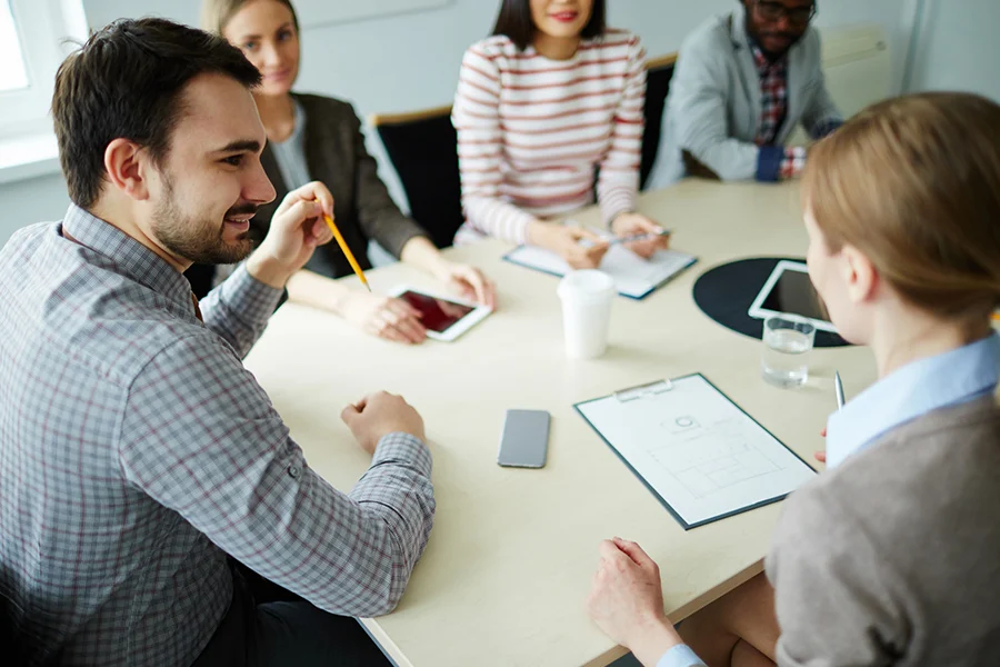 a group of professionals in a meeting discussing direct mail services, with documents, tablets, and notes on the table
