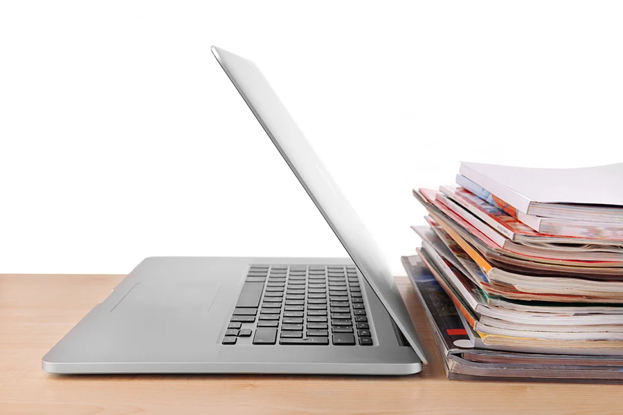 a laptop and a stack of magazines, illustrating the enduring strength of print advertising in the digital age