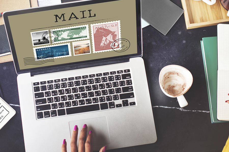 A person using a laptop displaying vintage postage stamps and mail graphics, representing direct mail design in a digital workspace