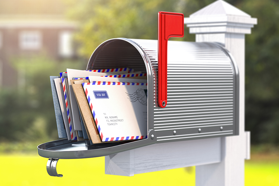 A traditional metal mailbox overflowing with envelopes, including airmail letters, representing direct mail advertising in a residential area