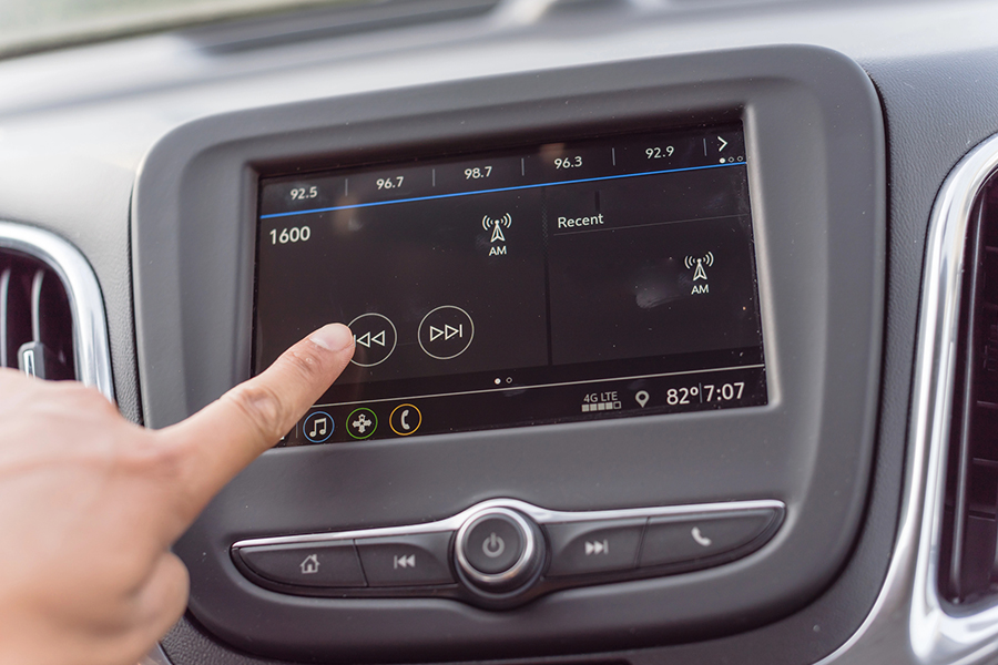 Close-up of a car's infotainment screen with a person tuning the radio, representing Satellite Radio Advertising opportunities