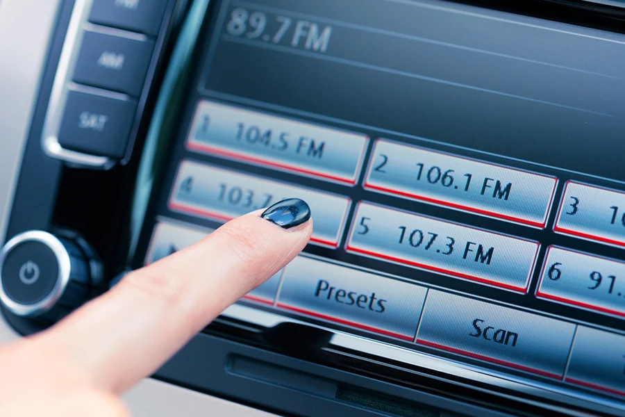 close-up of a person tuning a car's touchscreen radio to an fm station, highlighting the relevance of terrestrial radio advertising
