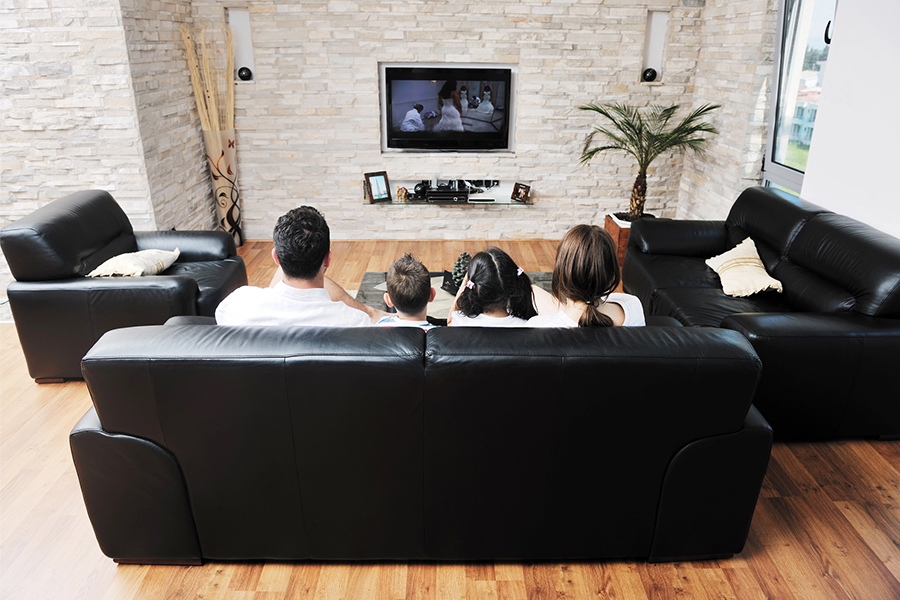 Family sitting on a black leather couch watching television in a modern living room, representing audience engagement with advertising on cable TV