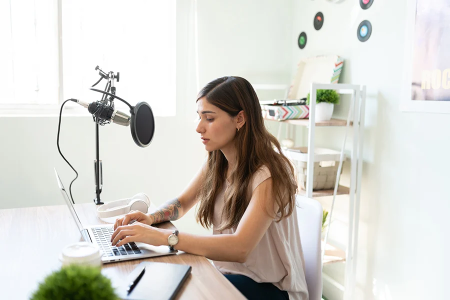 focused young woman working on a laptop with a professional microphone, creating content that showcases effective advertising through podcasts
