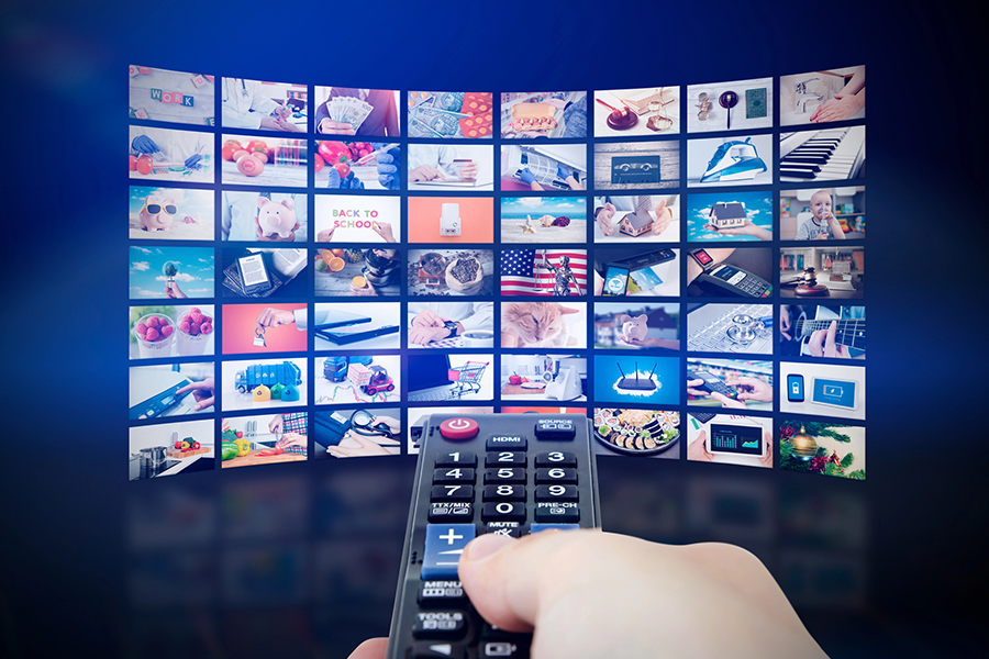 Hand holding a remote control in front of a large digital TV screen displaying multiple channels, representing Direct Response TV Advertising
