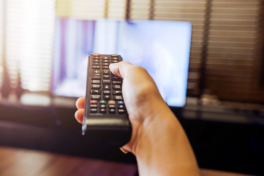 hand holding a remote control pointing at a blurred tv screen, representing network broadcast ads