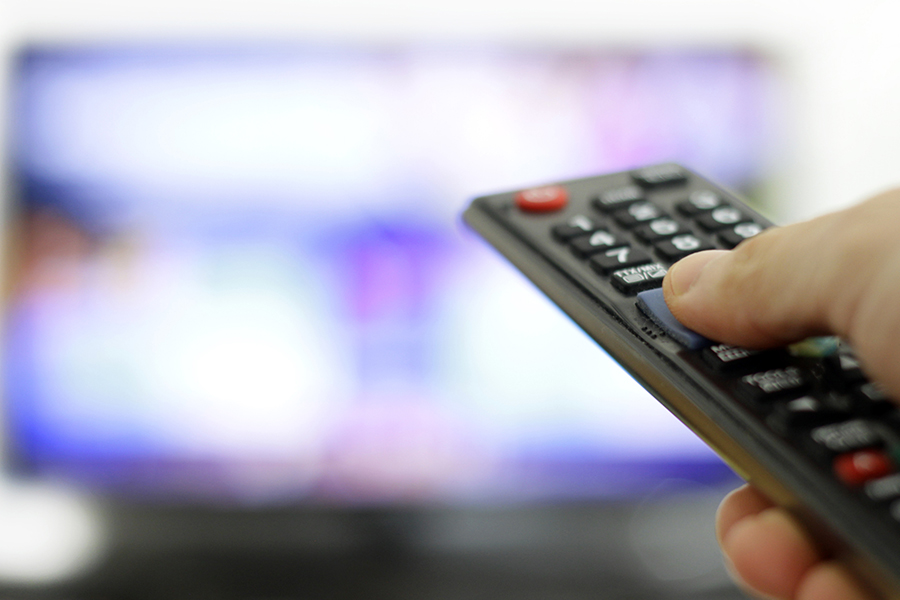 Hand holding a remote control pointing at a blurred television screen, illustrating the concept of cable TV advertising and viewer engagement