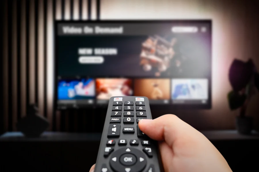 hand holding a remote control while browsing streaming tv programs on a screen