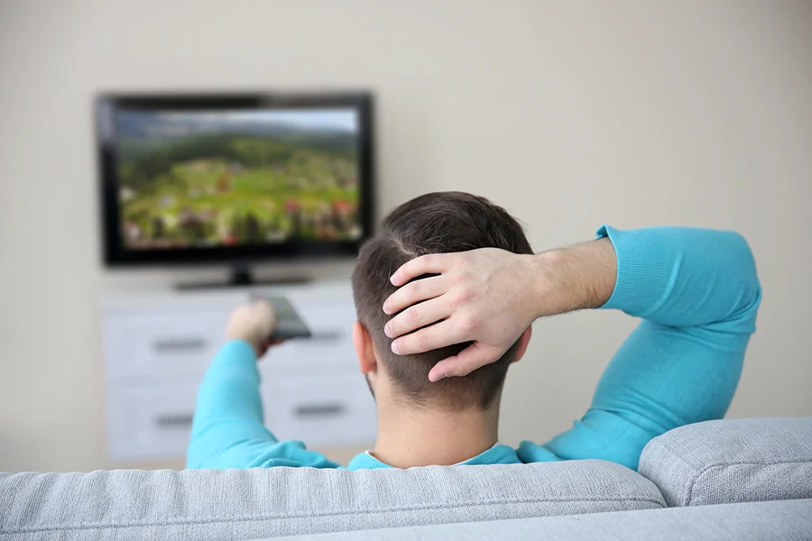 man relaxing on a couch, holding a remote while watching tv, representing audience engagement for a streaming tv ads agency