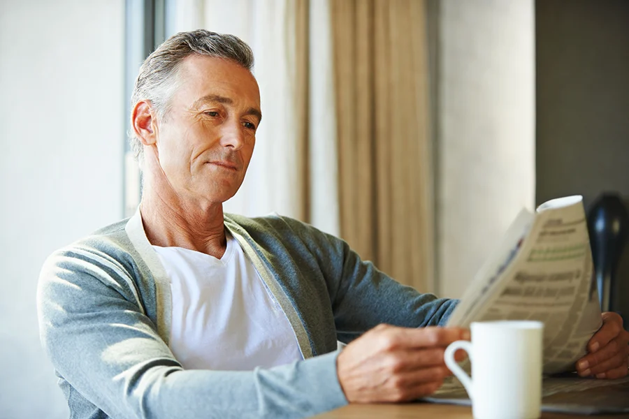 middle-aged man reading a newspaper with a cup of coffee, illustrating the impact of newspaper advertising on engaged readers