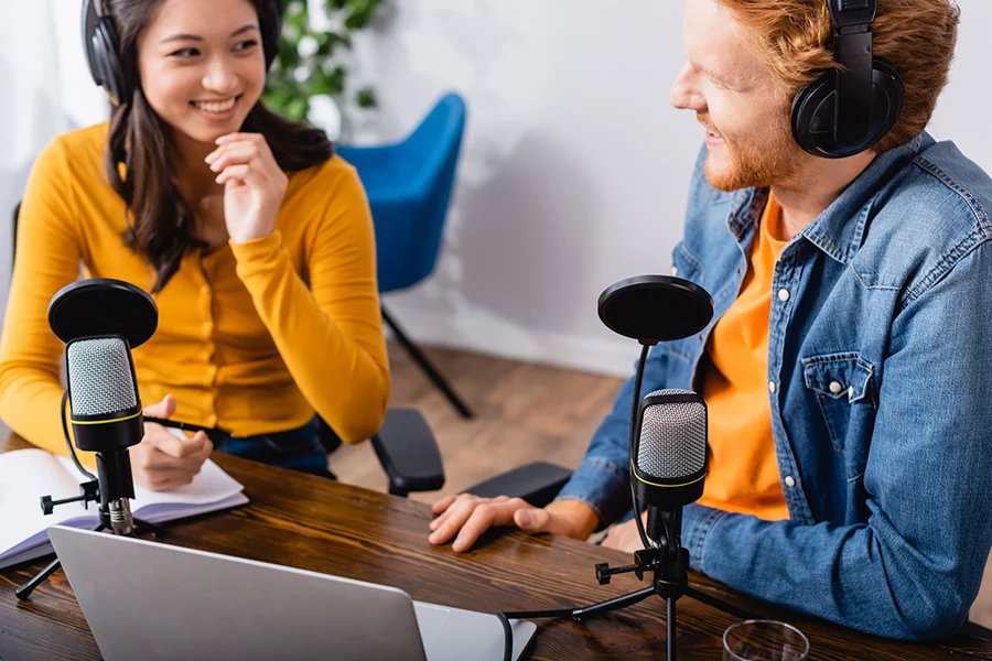 two radio hosts in a recording setup discussing audio advertising, wearing headphones and speaking into microphones