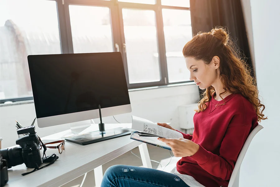 young woman reading a magazine at a modern workspace, highlighting the engagement potential of magazine advertising