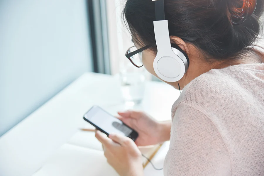 Young Woman Wearing Headphones And Using A Smartphone, Illustrating The Impact Of Streaming Audio Ads On Digital Engagement young woman wearing headphones and using a smartphone, illustrating the impact of streaming audio ads on digital engagement