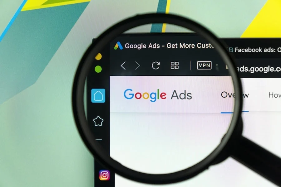 Google Ads Application Icon On Apple Imac Monitor Screen Under Magnifying Glass. a member of a franchise development marketing agency using a magnifying glass while setting up an ad campaign.