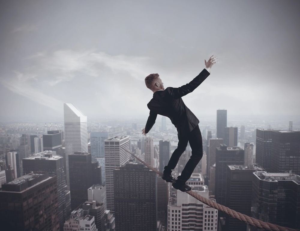 male business person walking over a city on a tightrope