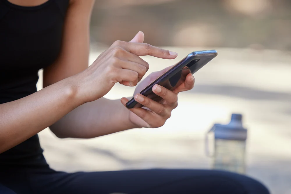 Smartphone, Fitness And Woman Hands With Outdoor Mobile App, Social Media Post And Website Blog Tips For Wellness, Nutrition And Training. Athlete Using Phone Or Cellphone Workout With A Water Bottle woman using her phone to book a medspa appointment on her phone due to medspa mobile optimization