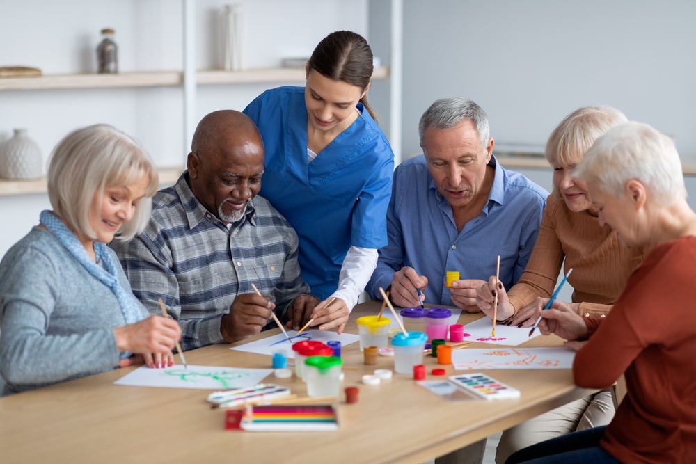 Senior living industry - A photo of cheerful creative multiracial senior men and women sitting around table and drawing at a senior living community, doing arts and crafts together.